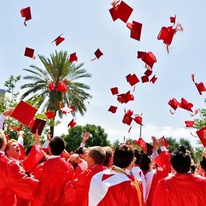 A group of people in red caps and gowns throwing their hats.